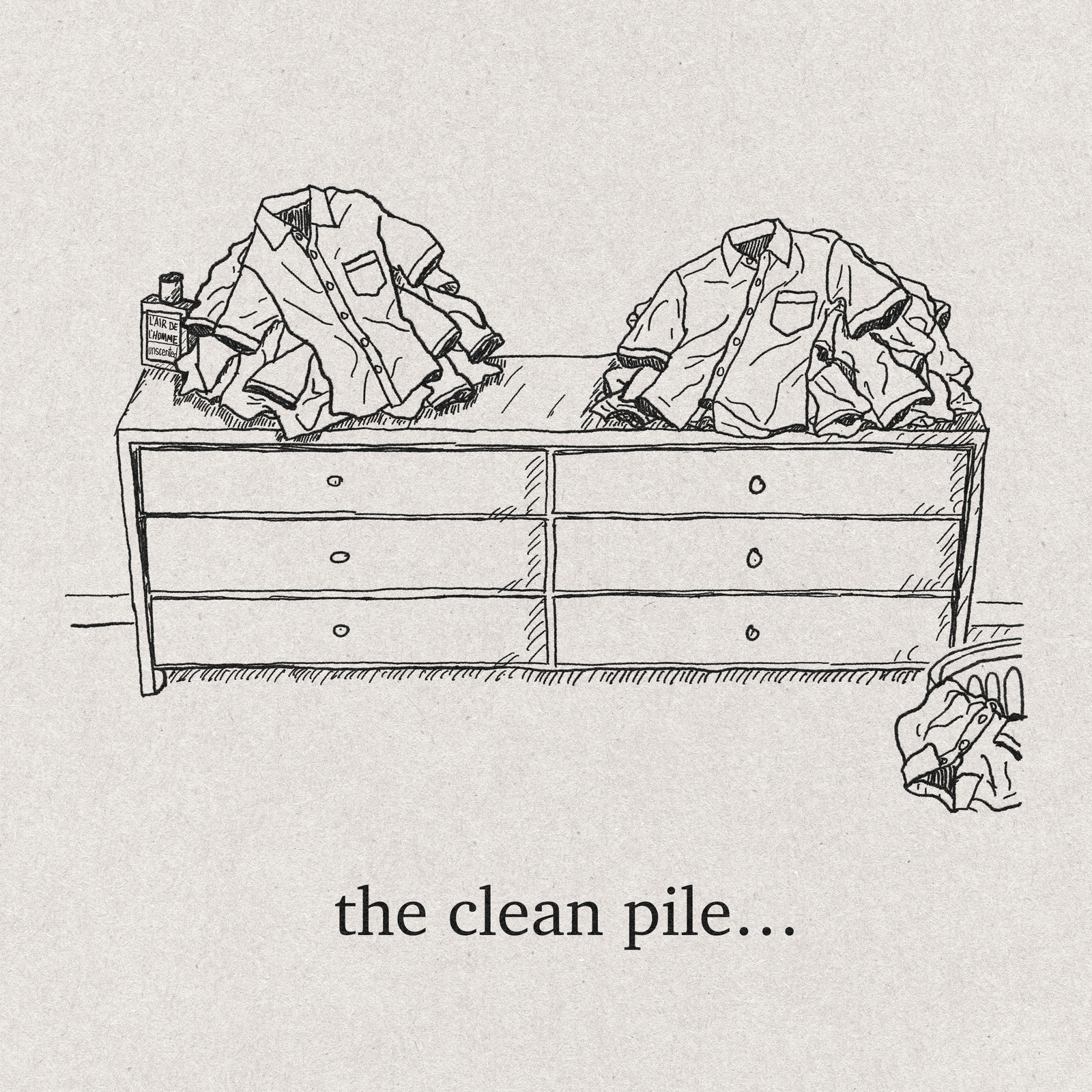 A long dresser seen straight on, six drawers closed. Two untidy heaps of identical short-sleeve work shirts sit on top, one at each end, with empty dresser between them. A small bottle labelled L'Air de l'Homme, unscented, stands half hidden beside the left heap. A laundry basket is cropped by the lower right edge of the frame. Caption: the clean pile…